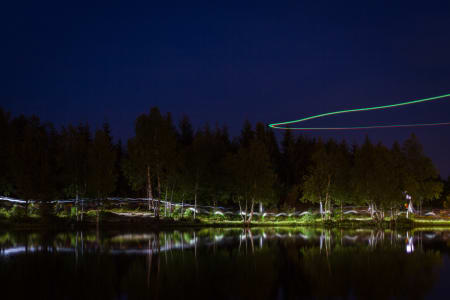 Hodelyktene danner kunstneriske striper langs vannkanten. Fra luften filmer en drone løperne.
