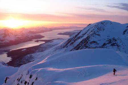 TROMS: Jiehkkevárri (også kjent som Jiekkevarri eller Jiekkevarre) er det høyeste fjellet i Troms på 1834 moh (Tromsø kommune). Toppen er kjennetegnet av en stor brekuppel som i tillegg til fjellets beliggenhet gjør toppen fysisk, men ikke teknisk, krevende å bestige. Fjellet er det høyeste og mest dominerende i Lyngsalpene, og kan sees på lang avstand. Mange mener at Jiehkkevarri på langs er den flotteste høyfjellstravers i Norge som du kan gjøre på en dag og blir av mange omtalt som «Norges Haute Route». Lengden er ca 30 km og antall høydemeter inntil 2400. Det er flere gode ruter opp, mens vi valgte å gå samme vei opp og ned via Holmbukttind. Jiehkkevarri utmerker seg ved at store deler av turen gir en utsikt en ikke er vant til. Fjell og hav om hverandre og i vårt tilfelle som startet 18 på kvelden, lystet av midnattsolen. Vi trasket totalt 12 timer på natten, var trøtte som fy da vi var ferdige, men høye så det holdt på naturopplevelsen! Det ble ikke mindre artig at vi gikk denne turen natt til 17. mai og fikk med oss feiringen i Tromsø by etter et par timer på øyet. Anbefaler alle som ikke har vært i Troms på vinterstid å reise hit – et eldorado for topptur! Vi gikk turen på randonee, men jeg har hørt mange har gått traversen på fjellski.
